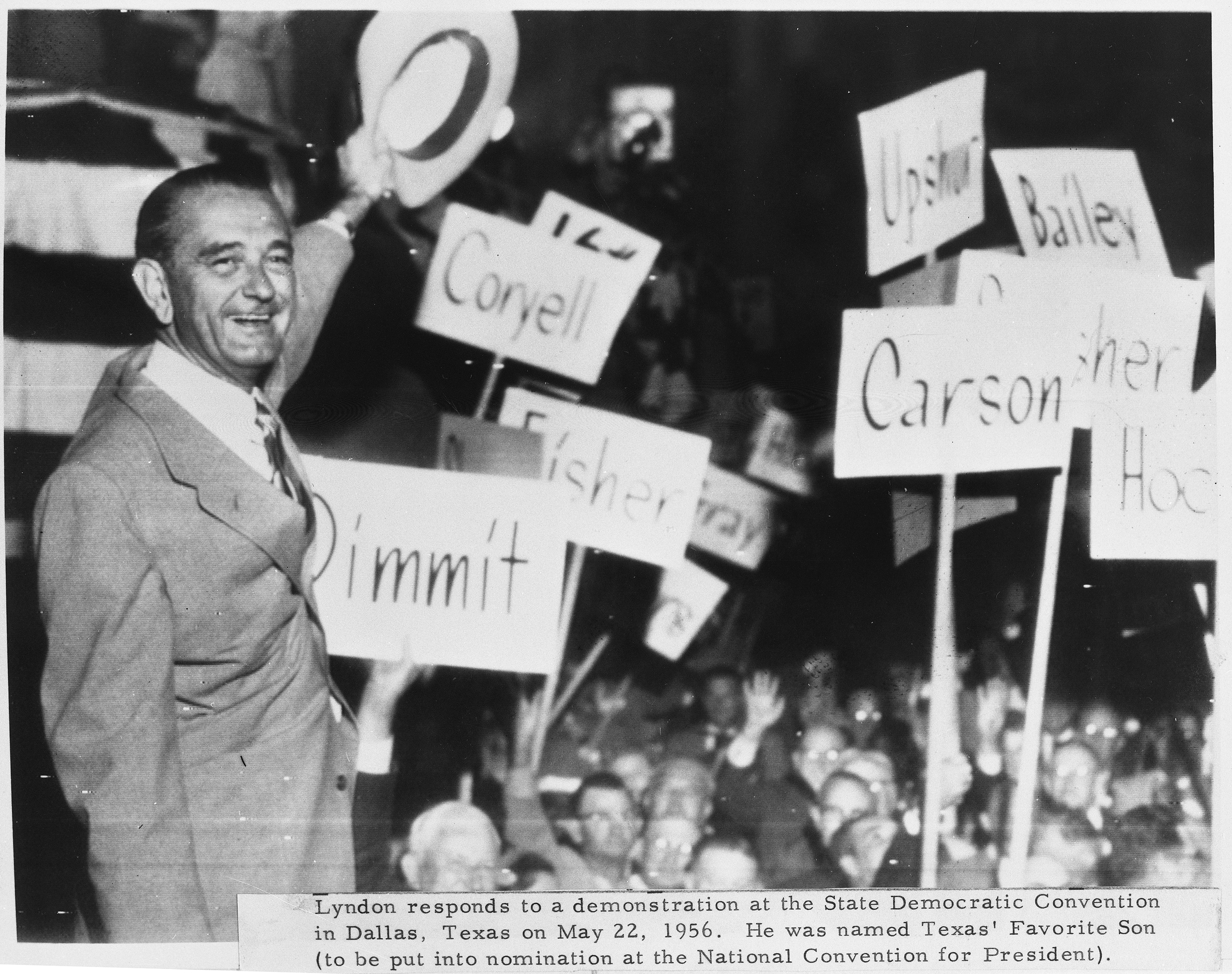 LBJ waves his hat to conventioneers holding signs with names of Texas counties.